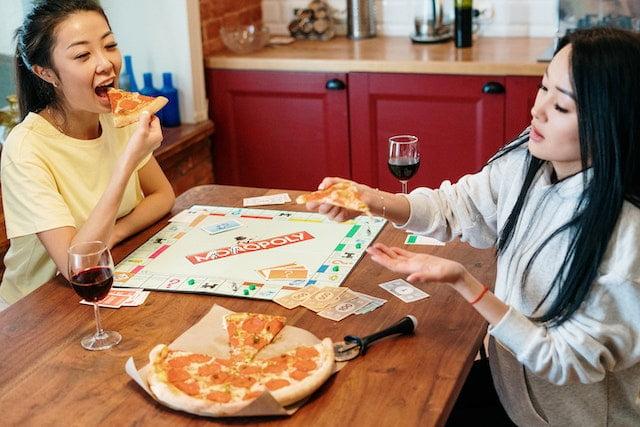 What Board Games Were Popular in the 1970s, women enjoying pizza while playing monopoly